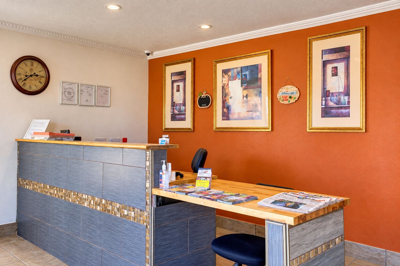 Una recepción con un reloj, certificados enmarcados y una pared decorada con obras de arte.