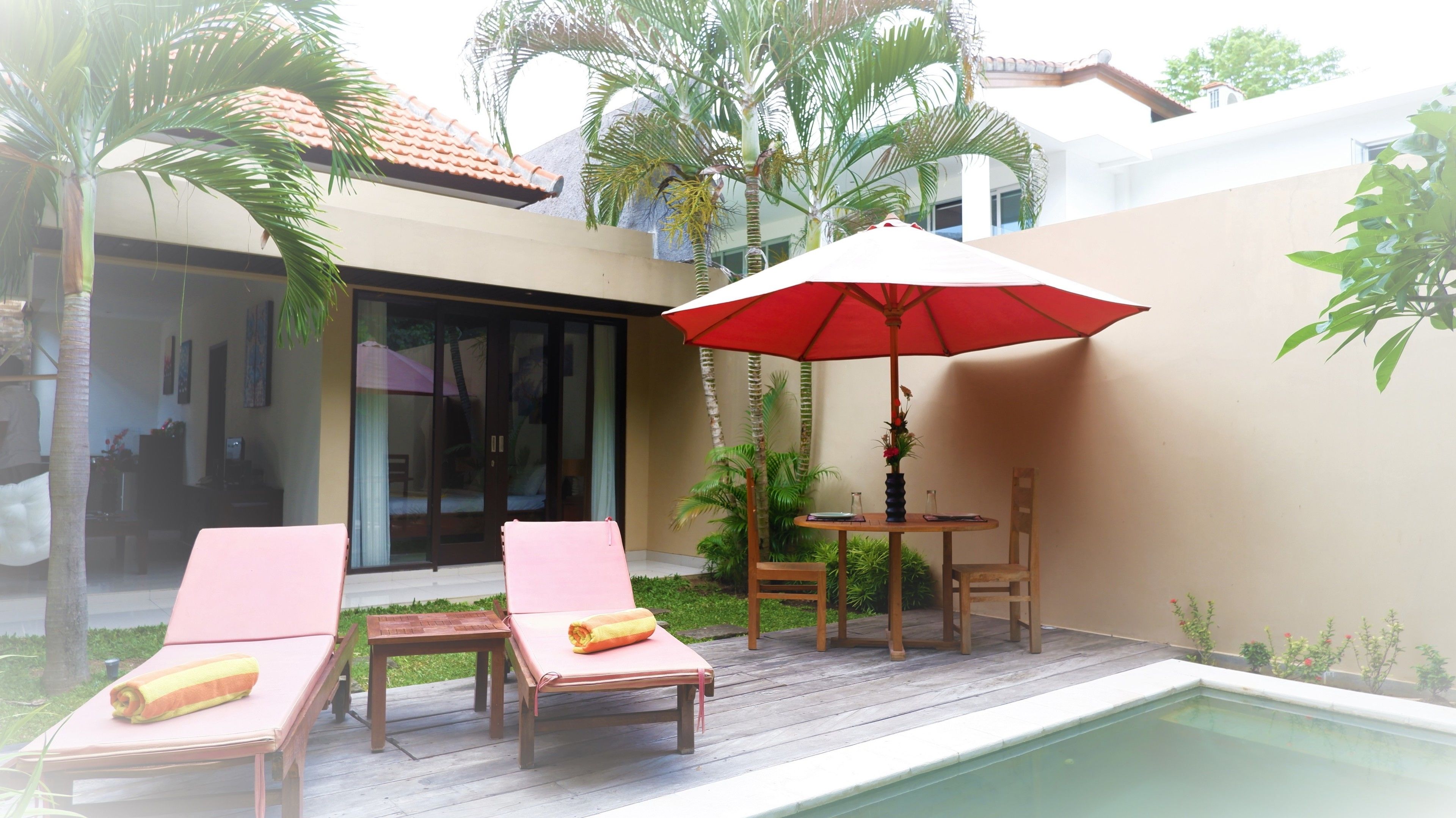 Un área junto a la piscina con dos tumbonas, una mesa con sombrilla roja y una silla.