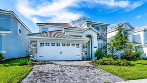 A suburban two-story house with a white garage door, a stone facade, and a tiled roof.