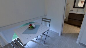 A small dining area with a white table and chairs, a bowl of fruit on the table, and a view of a bathroom with a mirror and sink. - Studio Colonel - Sleeps 4 (Castelsarrasin)