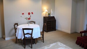 A dining area with a round table, chairs, a vase with flowers, a lamp, and a statue on a stand. - Studio Colonel - Sleeps 4 (Castelsarrasin)