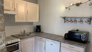 A compact kitchen with white cabinets, a built-in oven, a dishwasher, a coffee maker, and a toaster.