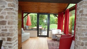 A covered patio area with stone walls, a white sofa, a red chair, and a table with an umbrella.
