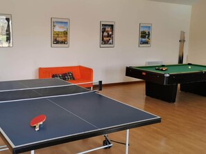A billiards table, a pool table, and a ping pong table in a room with a wooden floor and a sofa.