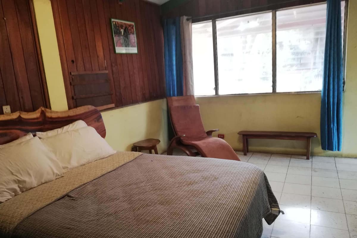 Una habitación de hotel con cama, una silla, una mesita y una ventana con cortinas.