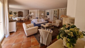 A spacious living room with a sofa, chairs, a dining area, and a kitchen in the background. - Villa 4 bedrooms, sleeps 300 meters from pampelone beach (Ramatuelle)