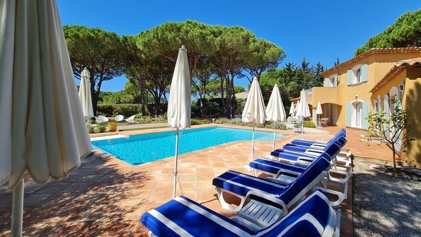 A pool area with lounge chairs and umbrellas, surrounded by trees and a building with a tiled roof. - Villa 4 bedrooms, sleeps 300 meters from pampelone beach (Ramatuelle)