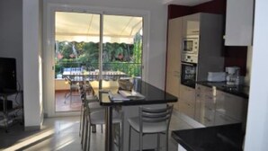 Cozinha moderna com área de jantar, grandes portas de vidro deslizantes que dão para uma varanda com vista para o verde.