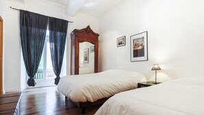 A hotel room with two beds, a wooden headboard, a mirror, framed pictures, a lamp, and a window with curtains. - Wonderful flat on the pear! (Nice)