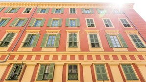 A multi-story building with a red and yellow facade, green shutters, and decorative moldings. - Wonderful flat on the pear! (Nice)