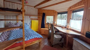 Een gezellig kamer in chaletstijl met een stapelbed, een houten bureau, rieten stoelen en een groot raam met uitzicht op bomen.
