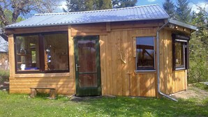 Een klein houten vakantiehuisje met een metalen dak, een voordeur en twee ramen.