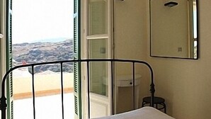A room with a bed, a window with a view of rocky terrain, a sink, and a mirror on the wall. - Apartments In Stenies, Andros, Cyclades Islands, Greece With Panoramic Views (Andros)