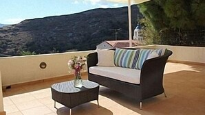 A balcony with a sofa, a small round table, and a vase of flowers. - Apartments In Stenies, Andros, Cyclades Islands, Greece With Panoramic Views (Andros)