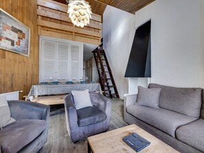 Un salon moderne avec une table à carreaux, des canapés en cuir, un plafond en bois et un escalier menant à une mezzanine.