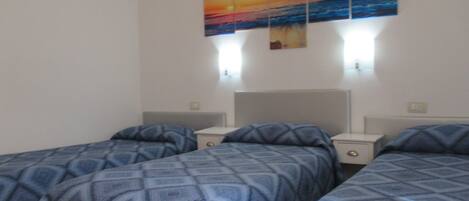 A hotel room with two beds, a nightstand, and a wall-mounted painting of a sunset over the ocean.