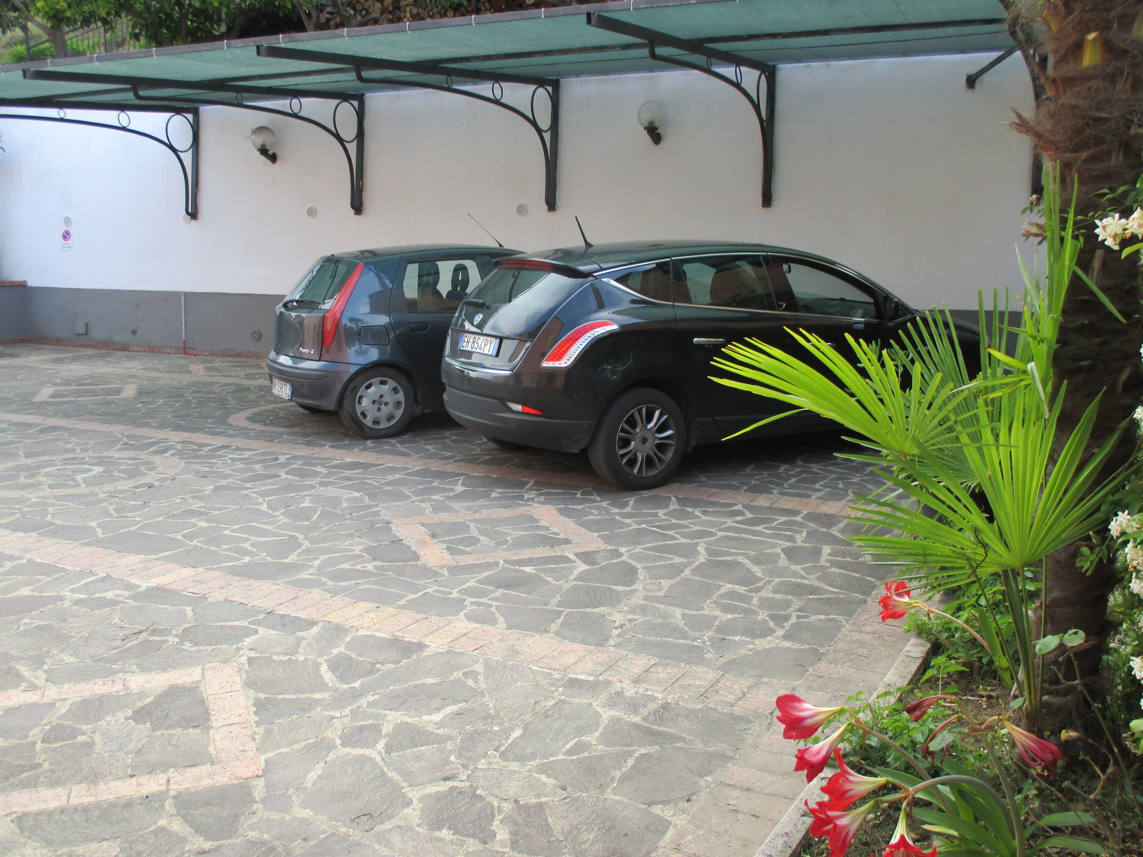 A parking area with two cars parked under a green awning.