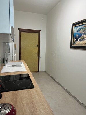 Eine Küche mit einer Holzarbeitsplatte, einem Spülbecken und einem Herd. Eine Tür mit Griff sowie ein Bild an der Wand sind ebenfalls zu sehen.