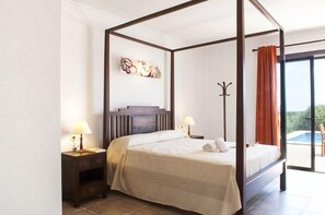 A four-poster bed with a headboard, two bedside tables with lamps, a wall art piece, and a view of the outdoors through a sliding glass door.
