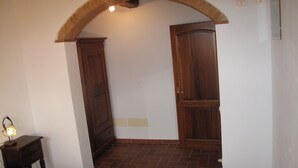 Una habitación con suelo de baldosas, un armario de madera, una puerta de madera y una mesita con una lámpara.