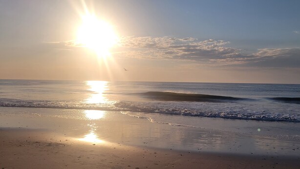 Ein Strand mit tiefstehender Sonne am Horizont, die ein warmes Licht über Wasser und Sand wirft.