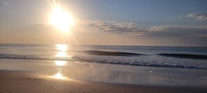 A beach with the sun low on the horizon, casting a warm glow over the water and sand.