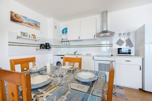 Une cuisine avec des meubles blancs, un four à micro-ondes et une table à manger pour quatre personnes.