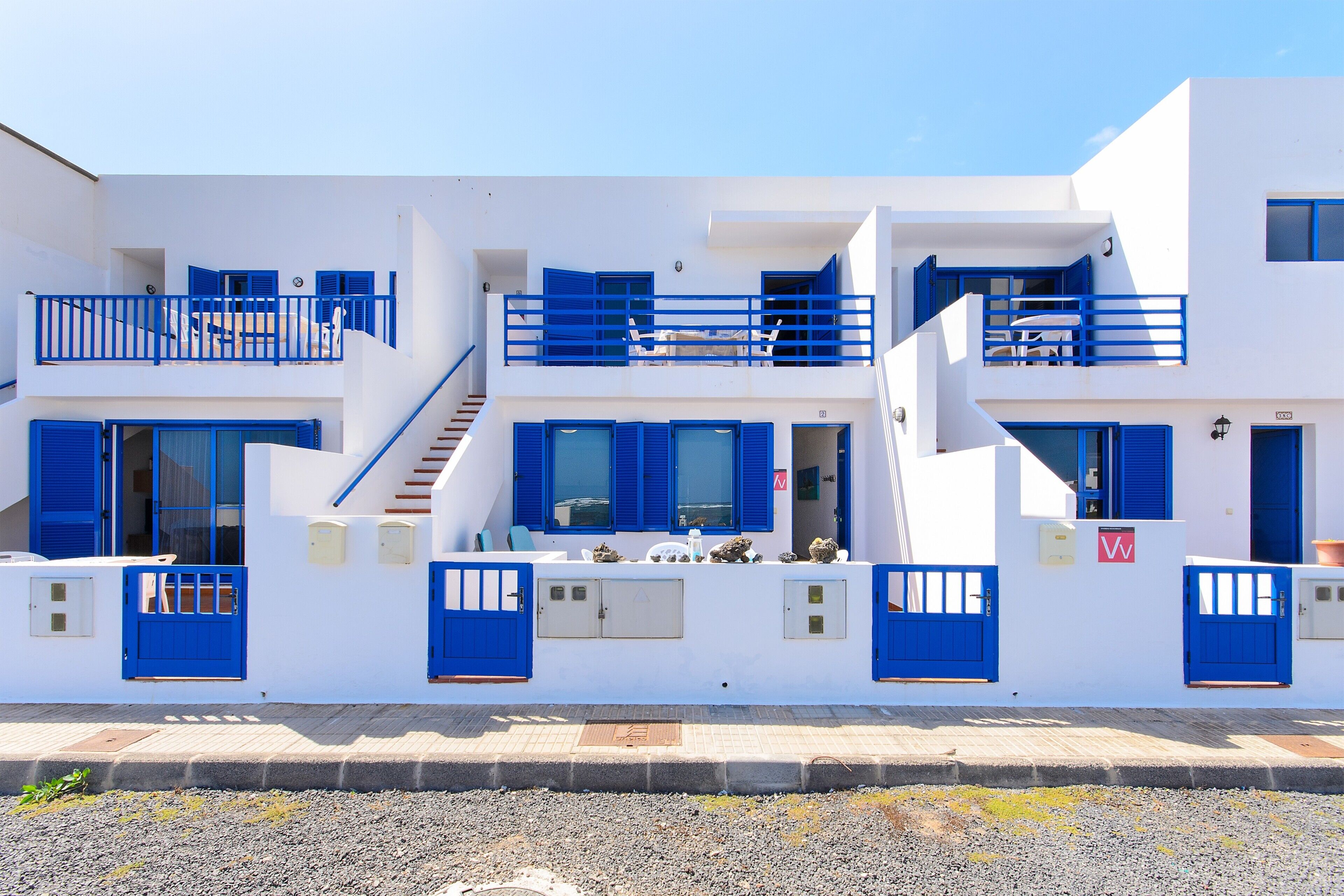 A white building with blue doors and windows, a staircase, and a balcony.