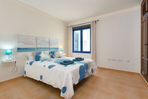 Une chambre à coucher avec un lit, une fenêtre, une table de chevet et une lampe fixée au mur.