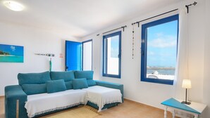 Une pièce avec un canapé bleu, une petite table avec une lampe et de grandes fenêtres avec des rideaux.