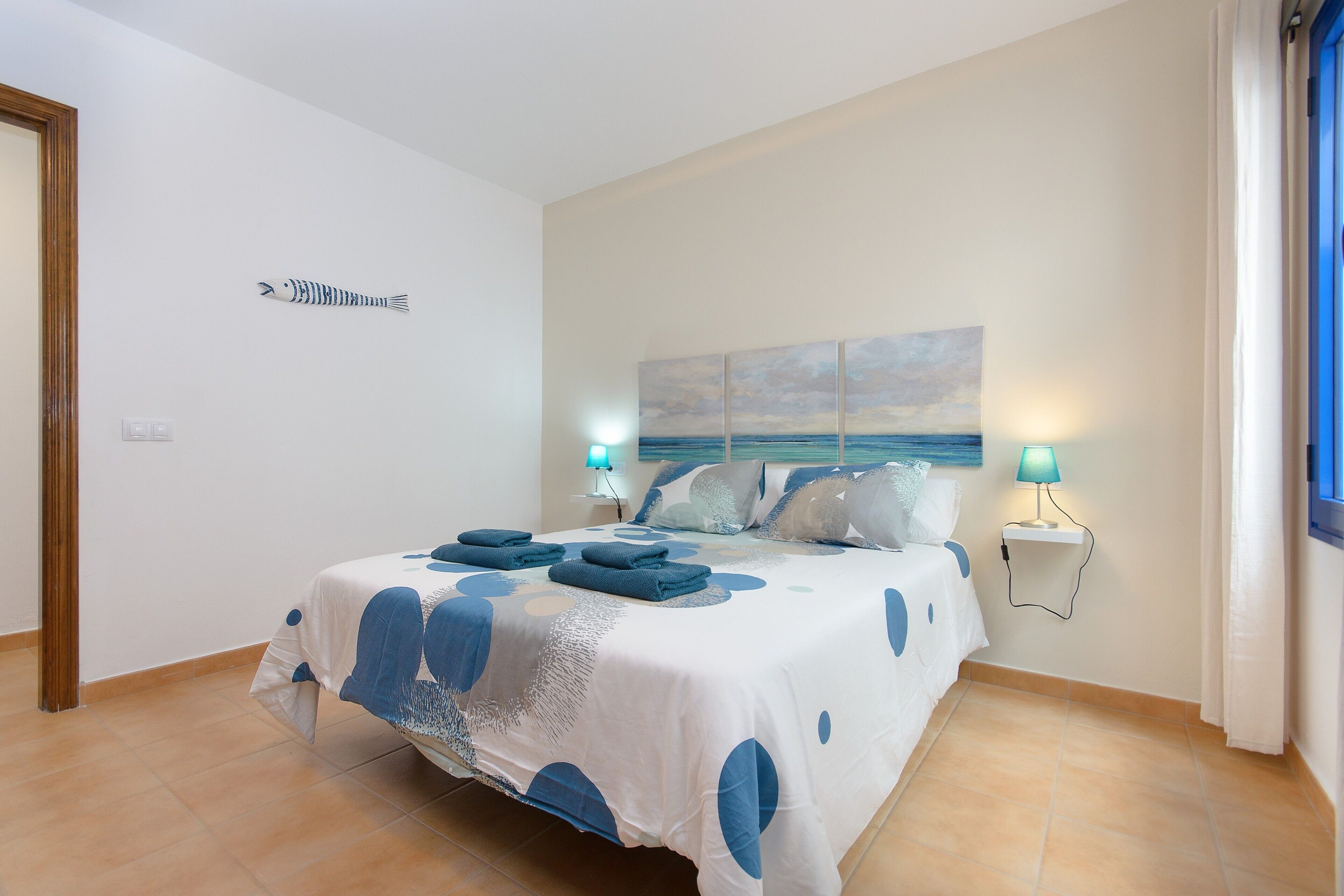 A bedroom with a bed, two bedside lamps, a wall-mounted artwork, and a door.
