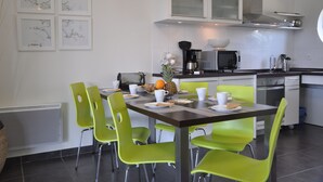 A modern kitchen with white cabinets, a microwave, and a coffee maker. There are green chairs around a table with plates and cups. - Calm, Nature, and the Sea, the ideal setting for your vacation! near Le Conquet! (Ploumoguer)