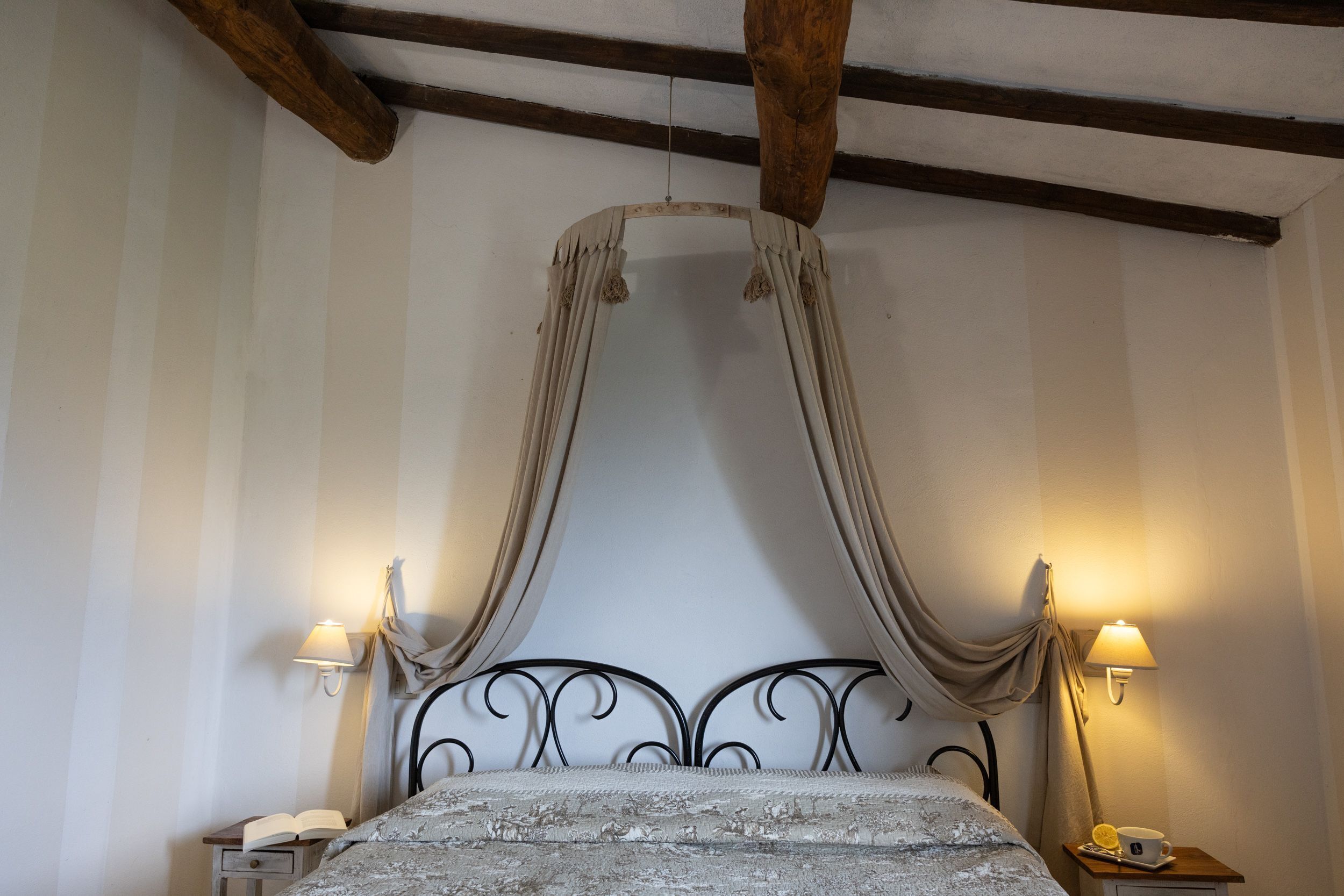 A bedroom with a canopy bed, two bedside lamps, a nightstand with a telephone, and a small table with a cup and a lemon.