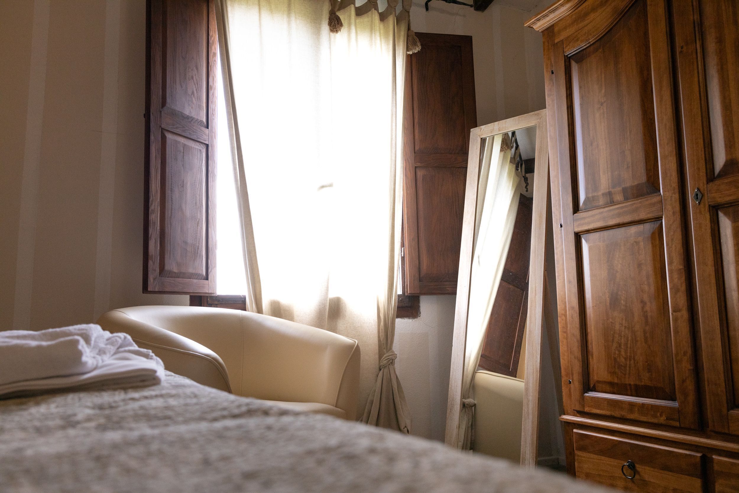 A bedroom with a bed, a chair, a wardrobe, and curtains.