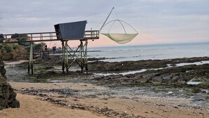 Ein Strand mit einer Holzkonstruktion, einem Fischernetz und felsigem Gelände.