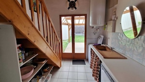 Eine kleine Küche mit einer Holztreppe, einem weißen Spülbecken und Blick ins Freie.
