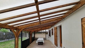 Ein überdachter Patio-Bereich mit Betonboden, Holzdecken und einem Tisch mit weißer Tischdecke.