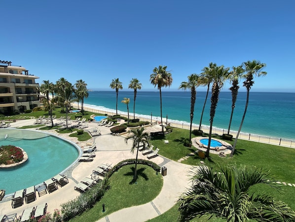 A resort with a pool, lounge chairs, palm trees, and a view of the ocean.