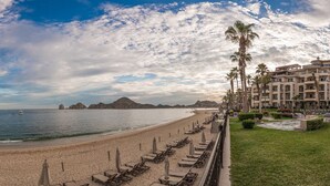 A beach resort with a long row of sun loungers and umbrellas, a pool area, and a view of the ocean and mountains. - Luxury 3br villa on Medano Beach w/resort amenities! (Cabo San Lucas)