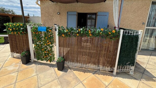 Una casa con patio piastrellato, una pergola, una recinzione ricoperta di piante rampicanti e un cartello blu.