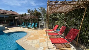 Una piscina con pavimento piastrellato, circondata da sdraio e un pergolato.
