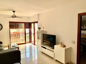 A living room with a TV, a sofa, a coffee table, and a sliding glass door leading to a balcony. - First line beach, free WIFI, air conditioning and garage # (El Médano)