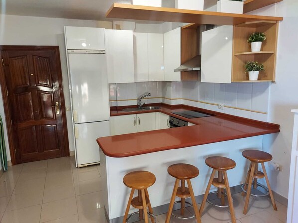 A kitchen with white cabinets, a red countertop, a built-in oven, a sink, and three wooden stools.