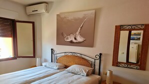 Un llit ben arrenjat amb un capçal trenat, una taula de nit amb una làmpada i un mirall fixat a la paret.
