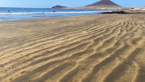 Una platja sorrenca amb onades suaus i una muntanya al fons.