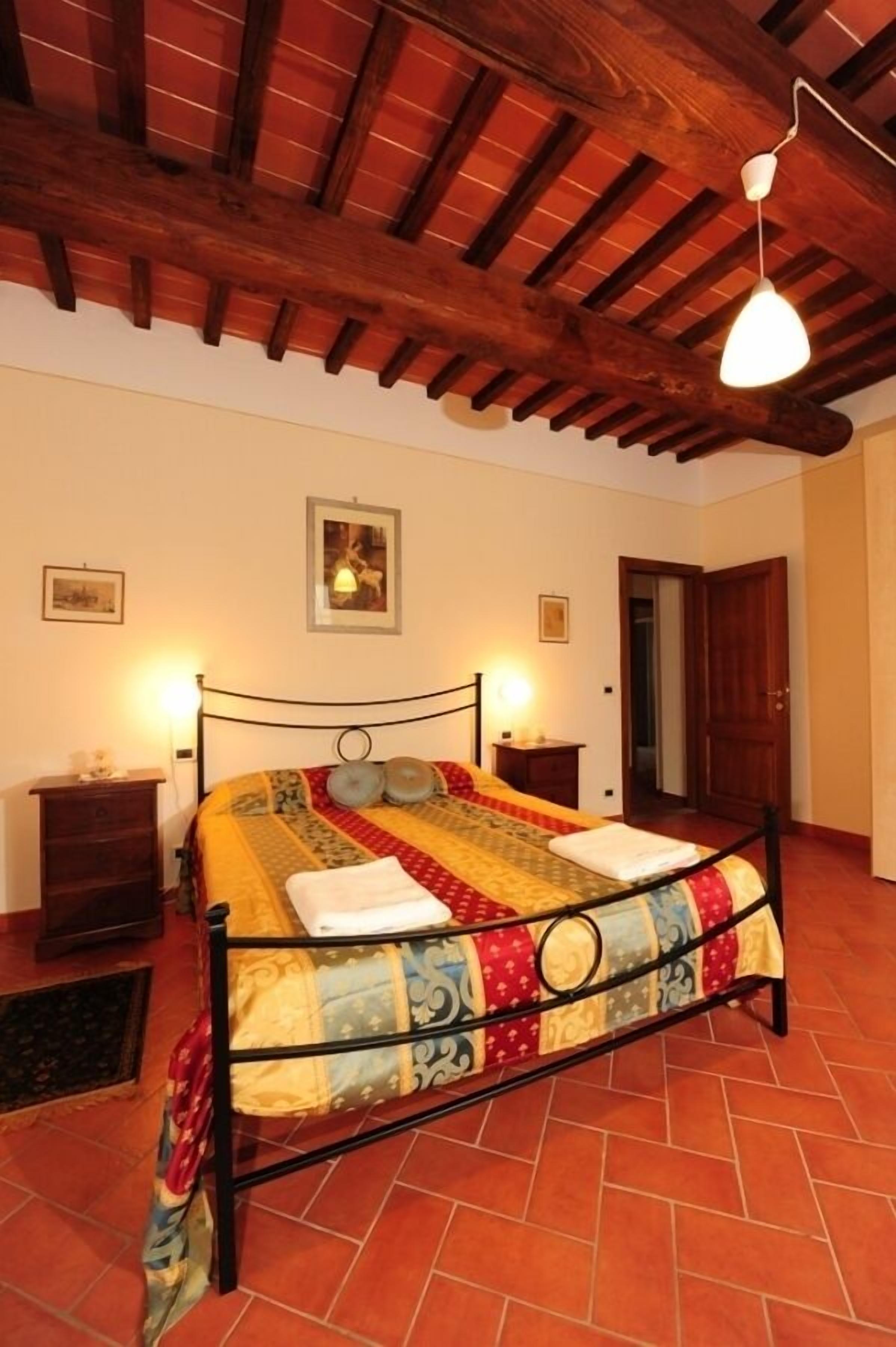 Un dormitorio con una cama, vigas de madera en el techo y dos lámparas de noche.