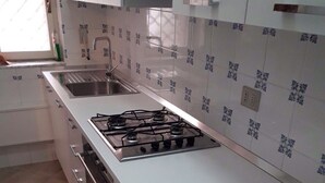 Une cuisine avec des meubles blancs, une cuisinière à gaz, un évier et des carreaux décoratifs.