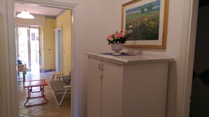 Un couloir avec une armoire blanche, un tableau représentant un champ et une petite table avec une chaise.