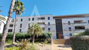 A modern building with multiple balconies, surrounded by palm trees and shrubs.