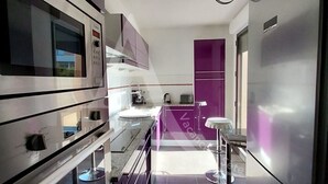 A modern kitchen with stainless steel appliances, a central island, and purple accents.